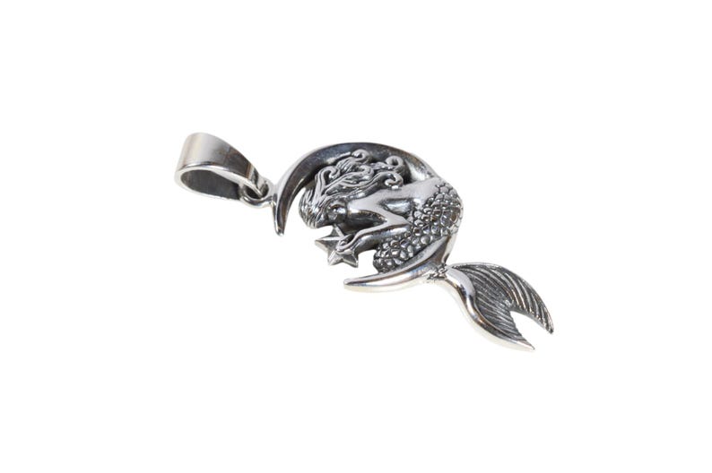 May include: A silver pendant featuring a mermaid curled around a crescent moon, holding a star. The pendant has a loop for attaching to a chain.