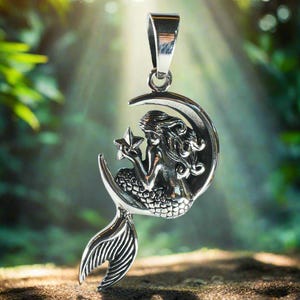 May include: A silver pendant featuring a mermaid sitting on a crescent moon holding a star. The pendant has a detailed design and is perfect for a necklace.
