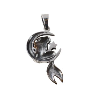 May include: A silver pendant featuring a crescent moon with a star and a stylized figure sitting on the moon.