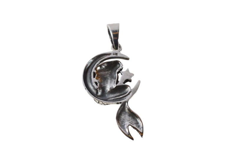 May include: A silver pendant featuring a crescent moon with a star and a stylized figure sitting on the moon.