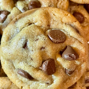 May include: Close-up of a golden-brown chocolate chip cookie with several chocolate chips. The cookie has a slightly uneven texture and is surrounded by other cookies.