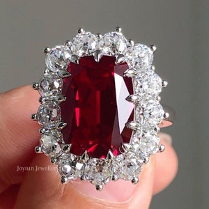 Peut inclure: Une bague en argent avec une grande pierre précieuse rectangulaire rouge entourée de petites pierres précieuses claires.