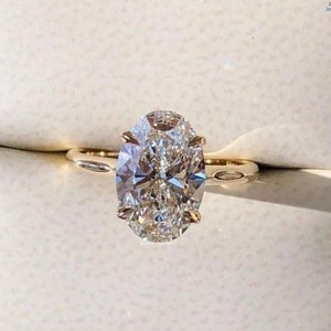 May include: A gold engagement ring with a large oval-shaped diamond. The diamond is set in a prong setting and has a halo of smaller diamonds around it.