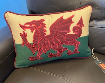 Puede incluir: Una almohada beige y verde con un dragón rojo bordado y una etiqueta blanca que dice "WALES".