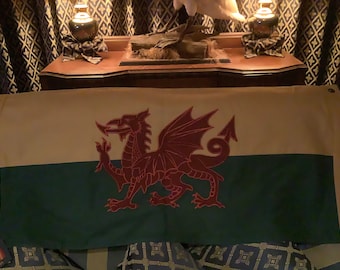 Puede incluir: Una bandera blanca y verde con un dragón rojo. La bandera está hecha de tela y tiene un dragón rojo sobre un fondo blanco con una franja verde en la parte inferior.