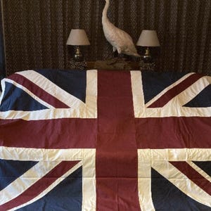 May include: A large rectangular Union Jack flag featuring the traditional design with a deep navy blue background, a central white cross, and a diagonal red cross outlined in white. The fabric displays visible seams and metal grommets on the side.