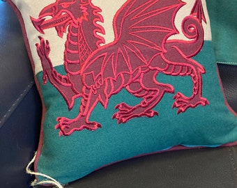 Puede incluir: Una almohada verde y blanca con un dragón rojo bordado. La almohada tiene una etiqueta que dice "W" con un diseño de rayas rojas y blancas.