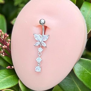 May include: A silver belly button ring with a butterfly charm and clear crystal accents. The ring is displayed on a pink mannequin.