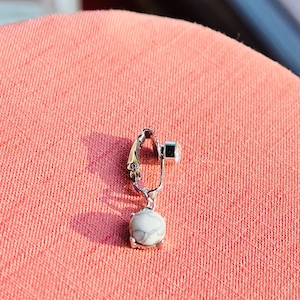 Puede incluir: Un pendiente de clip plateado con un colgante de piedra blanca. La piedra tiene un patrón de mármol.