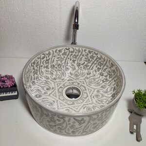 May include: A white ceramic sink with a grey floral pattern. The sink is round and has a single hole for a tap.