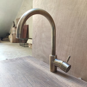 May include: A brushed nickel kitchen faucet with a single lever handle. The faucet has a high arc spout and is mounted on a wooden countertop.