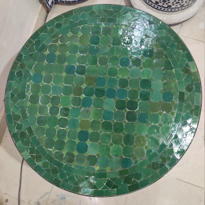 Pode incluir: Um tampo de mesa redondo de mosaico verde com um padrão geométrico. O tampo da mesa é feito de pequenos azulejos quadrados.