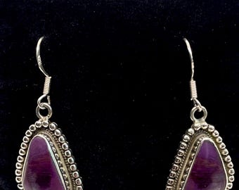 May include: A pair of silver earrings with a teardrop shape. Each earring features a polished, deep purple stone set within a beaded silver frame. The earrings hang from silver hooks, showcasing a classic design.