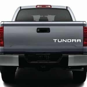 May include: A silver pickup truck with the word "Tundra" in white lettering on the tailgate.