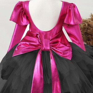 Puede incluir: Un vestido de tut&uacute; rosa y negro con un gran lazo rosa en la espalda. El vestido tiene mangas largas con volantes en los hombros.