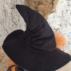 May include: Black witch hat with a tall, pointed crown and a wide brim. The hat is made of soft, plush fabric and has a gathered detail on the crown.
