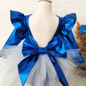 Puede incluir: Un vestido azul met&aacute;lico con un gran lazo en la espalda y una falda de tul blanco.