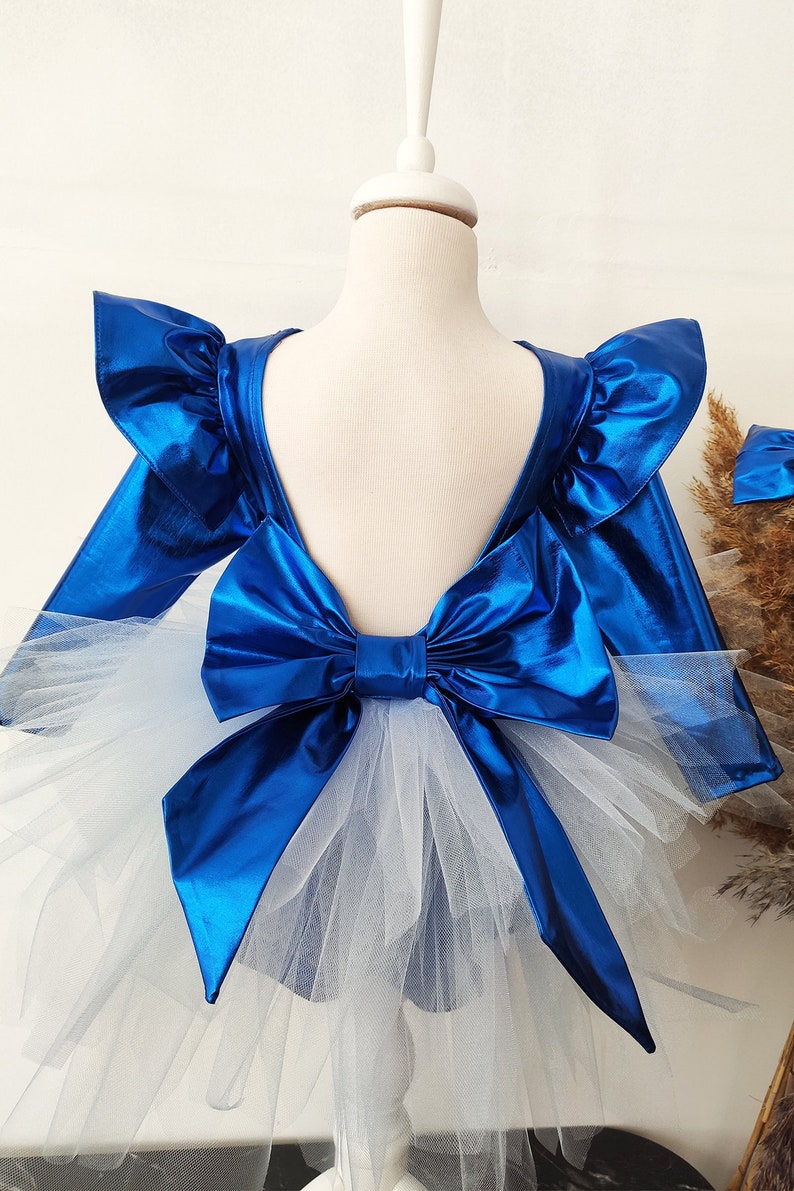 Puede incluir: Un vestido azul met&aacute;lico con un gran lazo en la espalda y una falda de tul blanco.