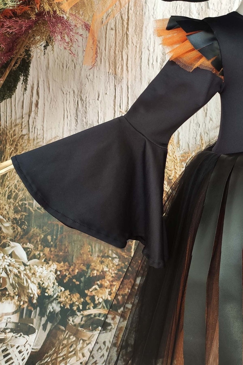 This witch costume for girls features a stylish design with black leather accents, black orange tulle, and a unique high-low hem, making it perfect for Halloween and special occasions