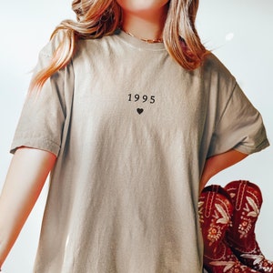 May include: A light brown oversized t-shirt with the year 1995 and a small black heart printed on the front.
