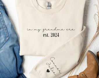 May include: A beige sweatshirt with the text "in my grandma era est. 2024" on the front and the text "Connor Julia" with a heart on the sleeve.