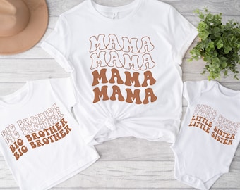 May include: A set of three white t-shirts with brown text. The largest shirt says "MAMA" four times in a retro font. The smaller shirt says "BIG BROTHER" four times in a retro font. The smallest shirt says "LITTLE SISTER" four times in a retro font.