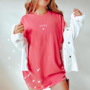 May include: A pink oversized t-shirt with the text "1995" and a small heart printed on the front.