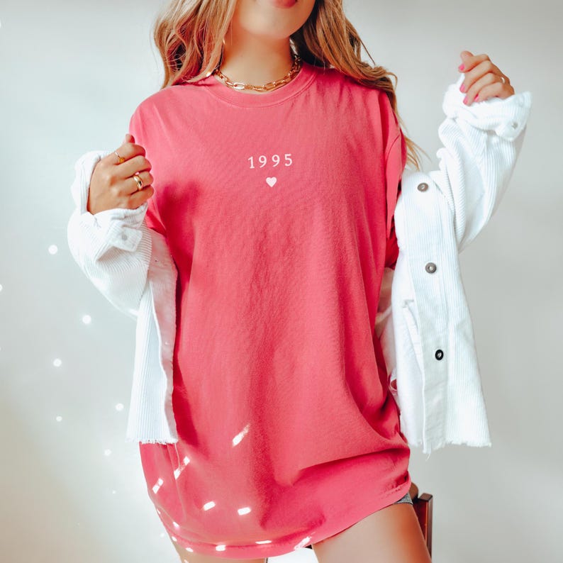 May include: A pink oversized t-shirt with the text "1995" and a small heart printed on the front.