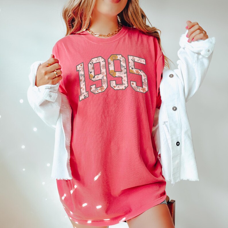 May include: A pink t-shirt with a floral print design of the year 1995.