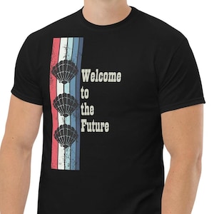 May include: Black t-shirt with a retro-style graphic featuring three seashells and the text "Welcome to the Future".