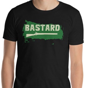 May include: Black t-shirt with the word "BASTARD" in white, above a green rectangle with a white rifle silhouette. The shirt is short-sleeved and made of a soft material.