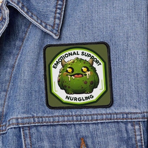 May include: A green and black embroidered patch with a cartoon monster and the text "Emotional Support Nurgling".