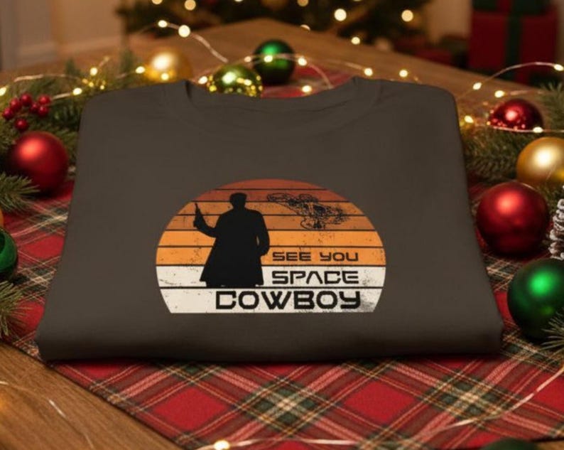 May include: A dark brown sweatshirt with a graphic design featuring a silhouette of a person holding a gun, a spaceship, and the text "SEE YOU SPACE COWBOY" in white. The design is set against a sunset background.
