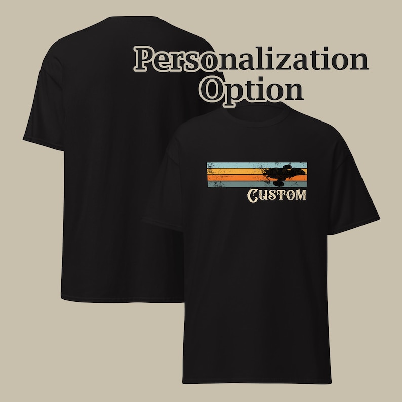 Op de afbeelding: Een zwart T-shirt met korte mouwen voorzien van een afbeelding met horizontale strepen in blauw, oranje en beige, een zwart silhouet van een voertuig en het woord CUSTOM eronder gedrukt. De tekst Personalization Option is boven het T-shirt zichtbaar.