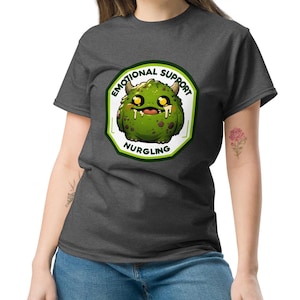 Puede incluir: Una camiseta gris oscuro jaspeada con un monstruo verde de dibujos animados que lleva una diadema blanca con el texto "Emotional Support Nurgling".