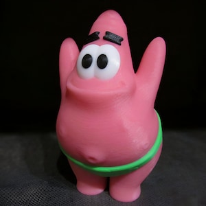 May include: A pink, three-dimensional figure of Patrick Star from the animated series Spongebob Squarepants. The figure has large white eyes with black pupils, black eyebrows, and a green band around the waist.