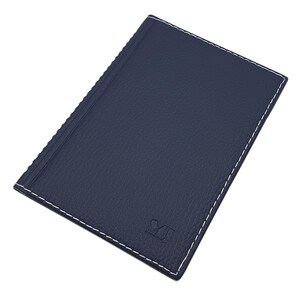 Könnte beinhalten: Ein marineblaues Leder-Notizbuch mit weißen Nähten an den Rändern. Das Cover hat eine strukturierte Oberfläche und ein geprägtes Logo in der unteren rechten Ecke. Das Notizbuch ist geschlossen und leicht angewinkelt.