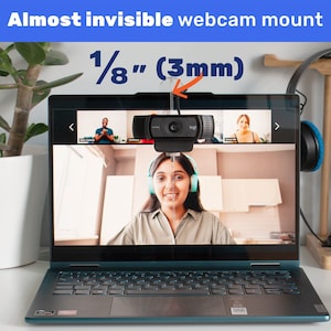May include: A black webcam mounted on the top of a laptop screen. The webcam is connected to the laptop with a thin black cable. The laptop screen shows a video call with three people. The text "1/8" (3mm)" is written above the webcam.
