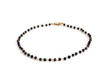 May include: A delicate necklace featuring a continuous strand of small, faceted black beads strung on a thin gold-toned wire. The piece is secured with a small gold-toned lobster claw clasp, creating a circular shape against a plain white background.