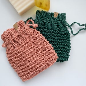 Könnte beinhalten: Zwei gestrickte Waschlappen, einer in hellrosa und einer in dunkelgrün. Beide Waschlappen haben ein Etikett mit dem Wort "Made" darauf.