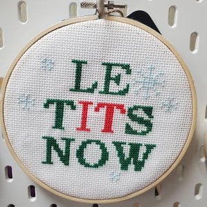 May include: A white embroidery hoop with a green and red cross-stitch design that reads "Let it snow".