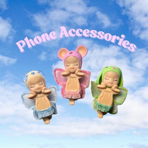May include: Three small figurines with closed eyes and angel wings, each wearing a different animal-themed hat: a blue dog, a pink mouse, and a green bunny. The text "Phone Accessories" is above them against a blue sky.