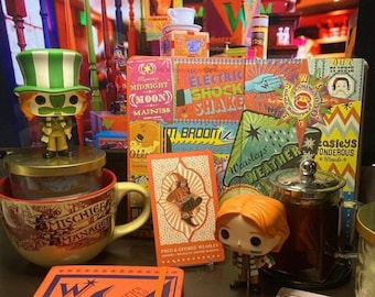 May include: A collection of Harry Potter themed items including a mug, a notebook, a book, a card game, and a figurine. The items are all orange and purple with the words "Weasleys Wizard Wheezes" printed on them.
