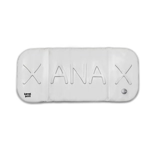 May include: White rectangular cushion with the word "ANAX" printed in black outlined letters. The cushion has two black X shapes on either side of the word.