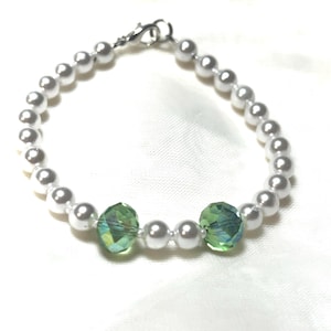 May include: A bracelet featuring a series of round white faux pearls interspersed with two faceted, translucent green crystal beads. The jewelry piece is secured with a silver-toned metal lobster claw clasp and a small circular jump ring connector.