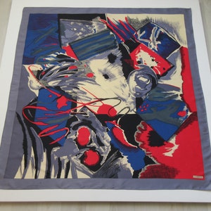May include: A silk scarf with an abstract design featuring bold colors like red, blue, black, and white. The design is made up of geometric shapes and lines.