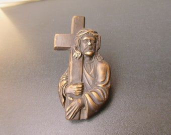 May include: A bronze-colored sculpture of Jesus carrying a cross. The sculpture is detailed and shows Jesus's face, hair, and clothing.