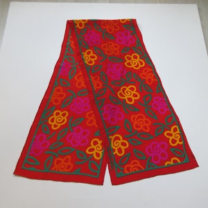 Könnte beinhalten: Ein roter Seidenschal mit einem floralen Muster in Orange-, Rosa- und Grüntönen. Der Schal hat einen grünen Rand und der Text "Emilio Pucci" ist in der unteren rechten Ecke sichtbar.
