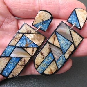 Könnte beinhalten: Ein Paar geometrische Ohrringe aus Holz und Perlmutt. Die Ohrringe sind blau, braun und weiß und haben ein geometrisches Muster.