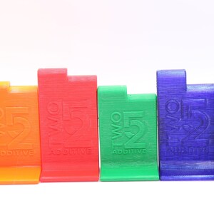 May include: Six colorful plastic blocks with the text "TWO 52 ADDITIVE" printed on each. The blocks are arranged in a row from left to right in the following order: yellow, orange, red, green, blue, and black.